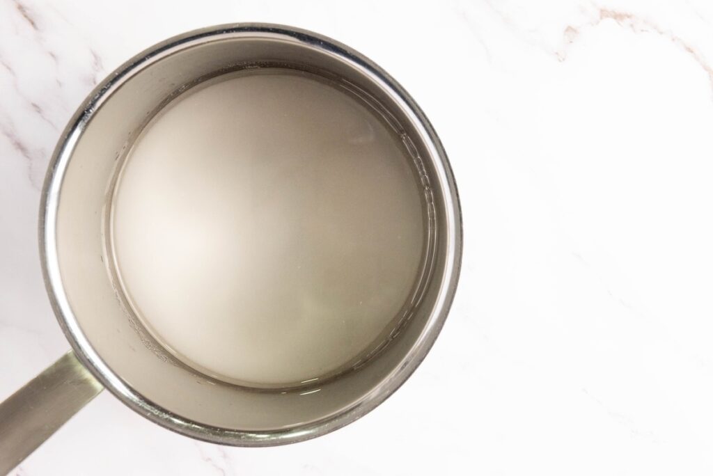 Overhead shot of a saucepan with clear, fully dissolved sugar syrup, ready for cranberries to be added