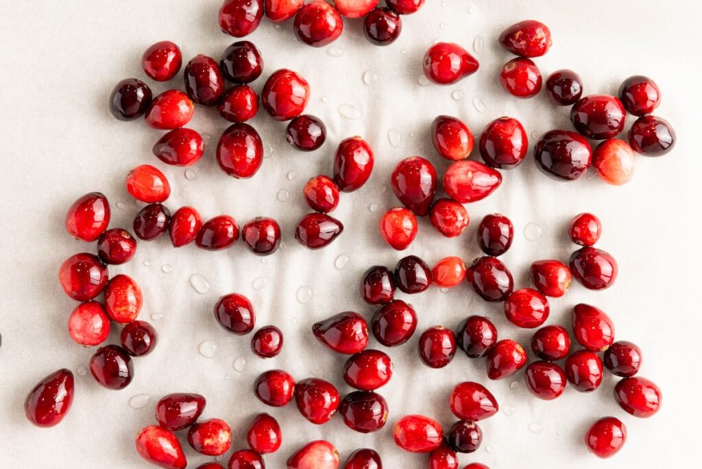 Cranberries resting on a parchment-lined tray, glistening with moisture after being soaked in syrup, prepped for sugaring