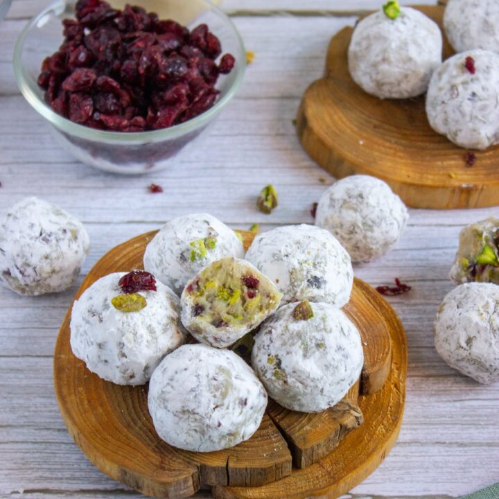 cranberry pistachio eggnog truffles on a wood plate with ingredients in the background
