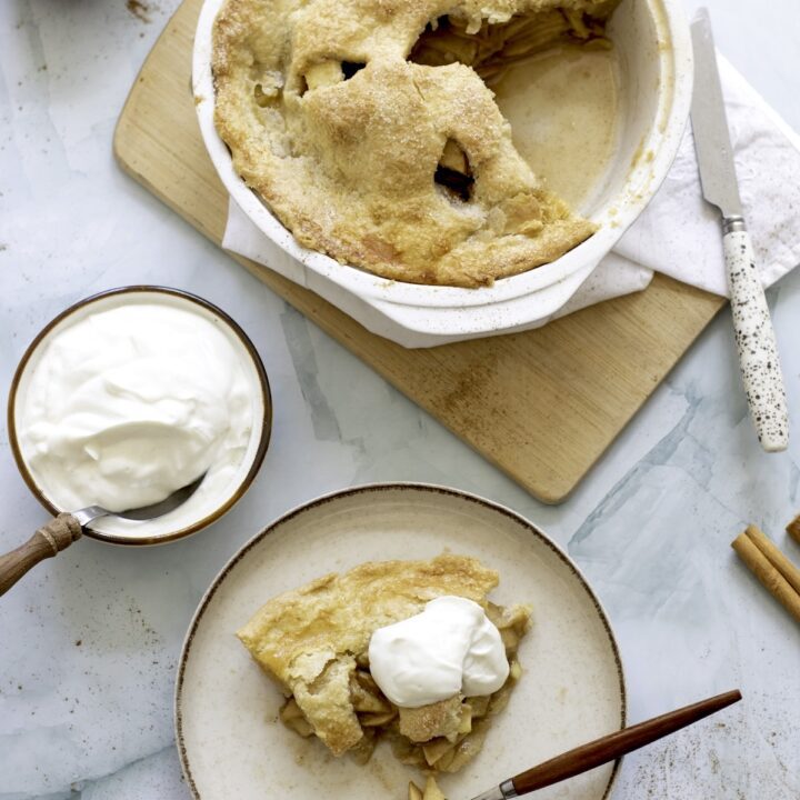 Aerial view of an apple pie with a piece cut out and a piece of apple pie on a plate with an ice cream scoop on top