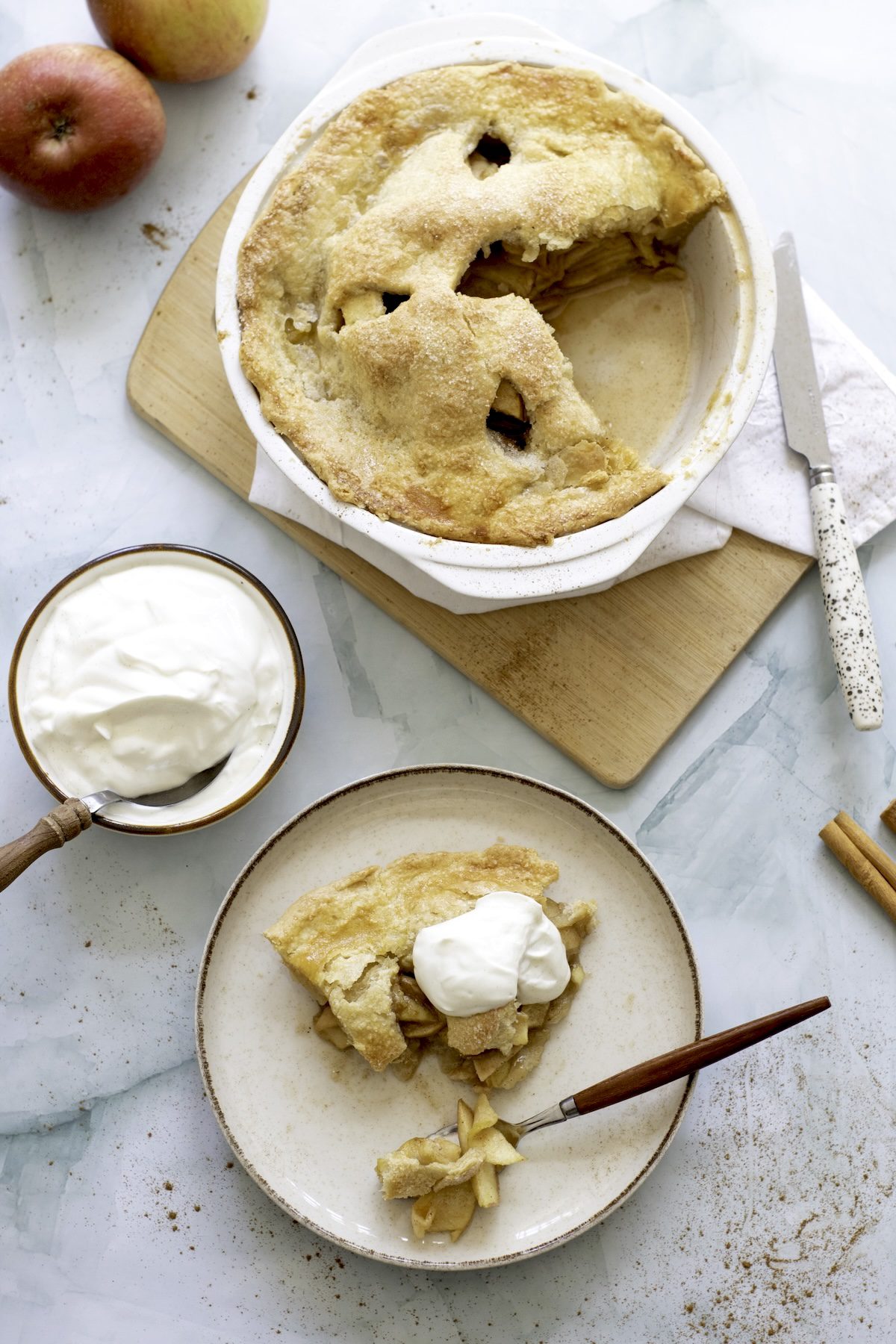 Aerial view of an apple pie with a piece cut out and a piece of apple pie on a plate with an ice cream scoop on top