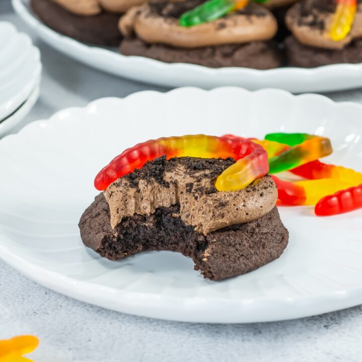 dirt cake cookies with a gummy worm on top, with a bite taken out on a plate