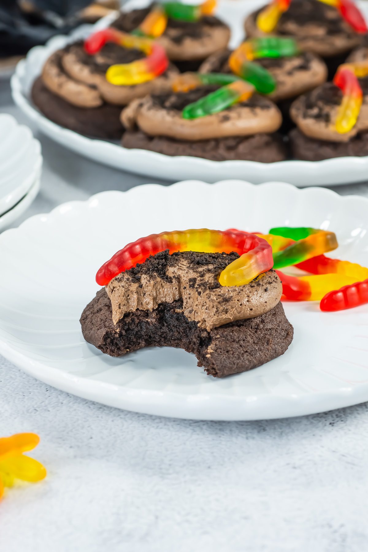dirt cake cookies with a gummy worm on top, with a bite taken out on a plate