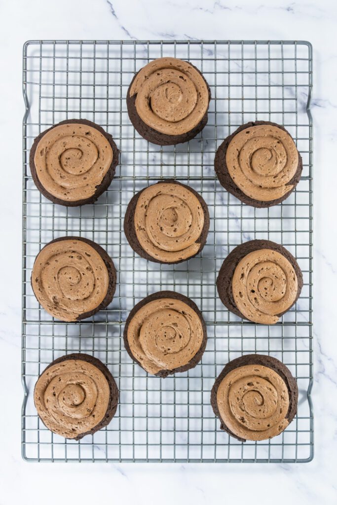 chocolate buttercream frosting piped in spirals on the top of chocolate cookies on a cooling rack