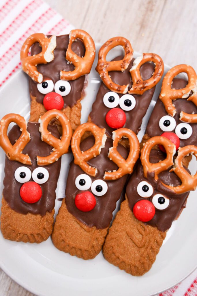 biscoff cookies half dipped in chocolate with pretzel antlers and candy faces to look like reindeer cookies