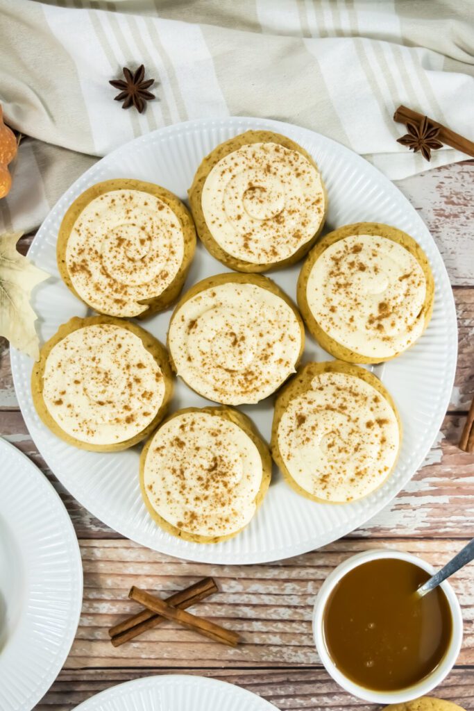 an overhead view of a plate full of caramel pumpkin cookies with frosting