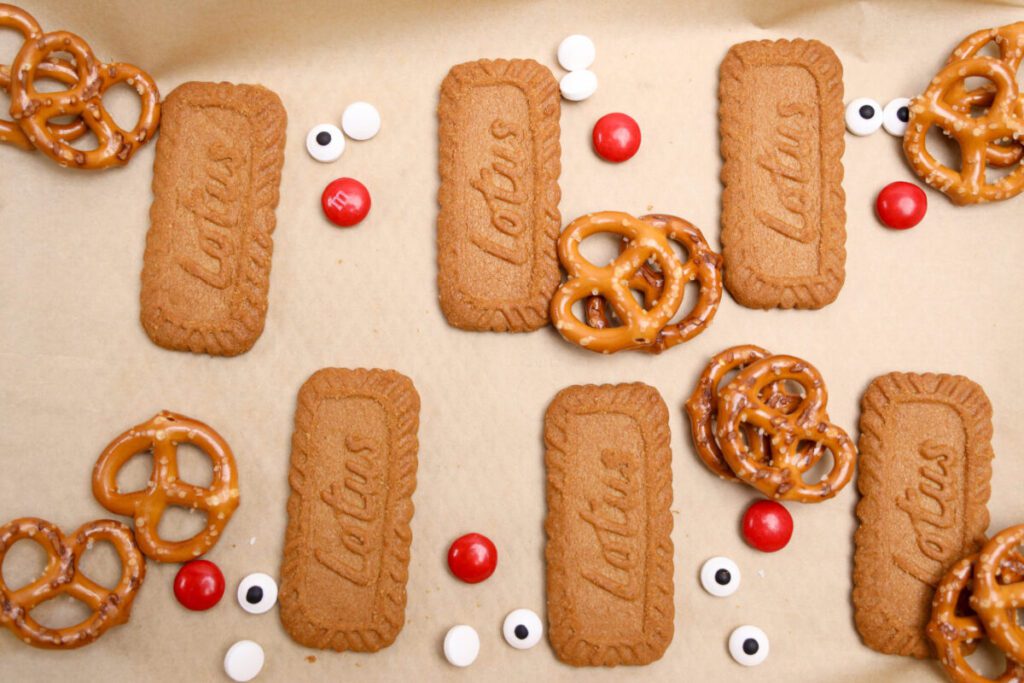 biscoff cookies on a tray with eye sprinkles, pretzels and red candies to make rudolph cookies