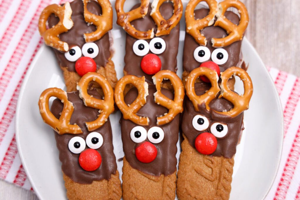 biscoff cookies half dipped in chocolate with pretzel antlers and candy faces to look like reindeer cookies